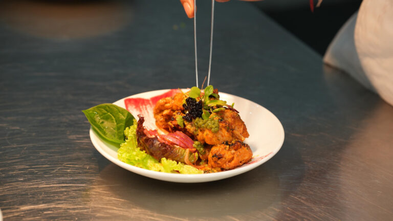 A chef finishing a kebab plate with tweezers