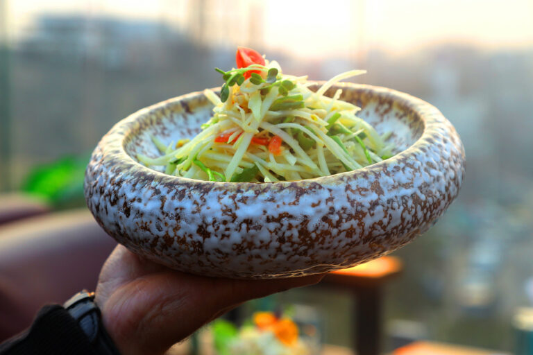 Raw papaya salad in a stone bowl, held to camera